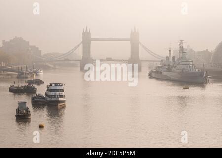 Tower Bridge with red London bus driving over it in London in foggy misty weather, with the River Thames in beautiful mysterious atmospheric light, shot in Coronavirus Covid-19 lockdown in England, Europe