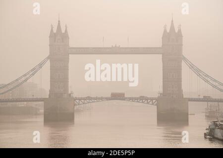 Tower Bridge with red London bus driving over it in London in foggy misty weather, with the River Thames in beautiful mysterious atmospheric light, shot in Coronavirus Covid-19 lockdown in England, Europe Stock Photo