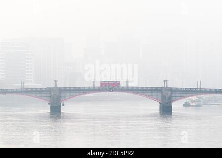 Central London City Skyline with iconic red London bus driving over Lambeth Bridge with misty foggy skyscraper buildings shot in Coronavirus Covid-19 lockdown in England, UK Stock Photo