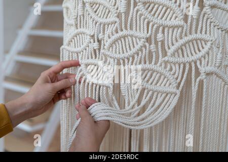 Freelancer woman working on half-finished macrame piece, weaves lamp shade for chandelier. Women hobby. Stock Photo