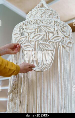 Freelancer woman working on half-finished macrame piece, weaves lamp shade for chandelier. Women hobby. Stock Photo
