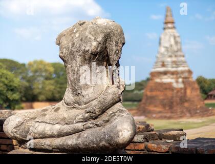 Headless and armless statue of Buddha seated in lotus position made of stone, stupa made of brick behind. Thai Buddhist temple in ruins, Wat Chaiwatth Stock Photo