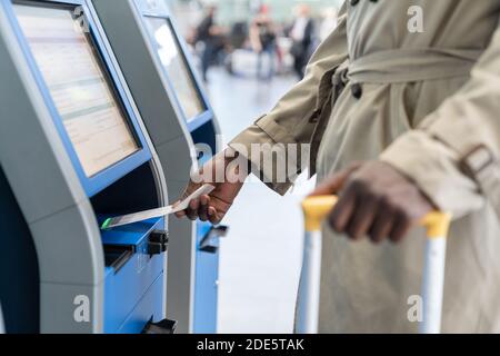 Black traveler man using self check-in machine kiosk service at airport, scans code on boarding ticket. Close up. Stock Photo