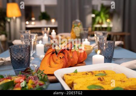 Part of served festive table with wineglasses, burning candles, vegetable salad, homemade grilled corn, baked pumpkin and other food Stock Photo