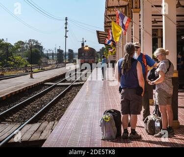 Thailand; Feb 2020: Group of foreign travelers waiting for a train at a Thai train station, senior backpackers wearing casual clothes, man with rasta Stock Photo