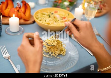 Hands of young African woman putting homemade pasta on her plate during Christmas or Thanksgiving dinner by served festive table Stock Photo