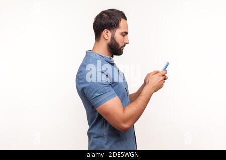 Side view serious assertive man typing on smartphone, betting, using online application, chatting in messengers. Indoor studio shot isolated on white Stock Photo