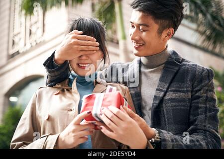 young asian man giving girlfriend a surprise present outdoors Stock Photo