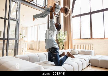 Loving african father jumping with little son on soft couch Stock Photo