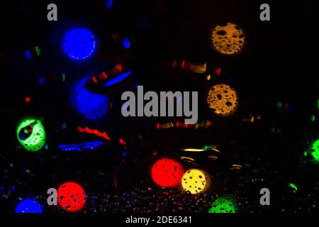 Colorful bokeh lights on a dark background behind the raindrops on the glass texture Stock Photo