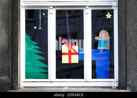 Dortmund, Germany, November 29th, 2020: Apartment window decorated for Christmas refers to Christmas Eve in Corona times. The man giving the gift wears mouth and nose protection against the virus. Stock Photo
