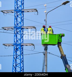 Uniformed electricians repairing electrical wires on a high pole Stock Photo