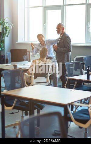 Group of happy coworkers talking, discussing something and smiling while working together in coworking space, vertical shot Stock Photo