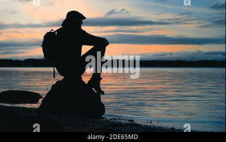 Silhouette of a man sitting on a rock, looking at the sea Stock Photo