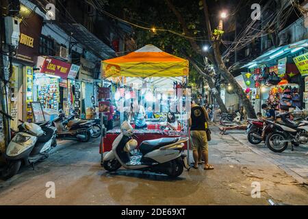 Street vendors and retail shops selling different merchandise in a night market in Hanoi Old Quarter, Vietnam Stock Photo