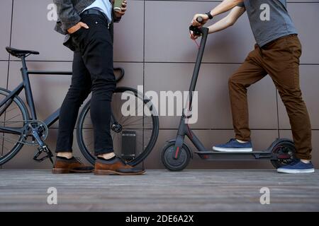 Colleagues. Cropped shot of two co workers in casual wear standing outdoors with eco friendly transport bicycle and electric scooter Stock Photo