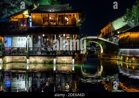 Night time view of people eating and socialising in a waterfront restaurant in Wuzhen West Scenic Zone water town, Zhejiang, China Stock Photo