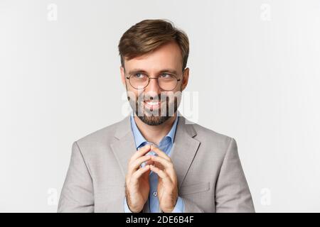 Close-up of thoughtful and devious businessman having an idea, smiling cunning and looking at upper left corner, steeple finers and scheming something Stock Photo