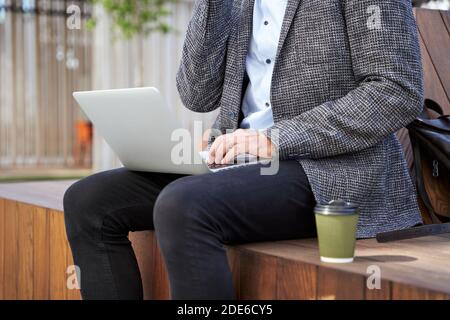 Cropped shot of busy elegant mature man talking on the phone, working on his laptop while sitting on the bench outdoors Stock Photo