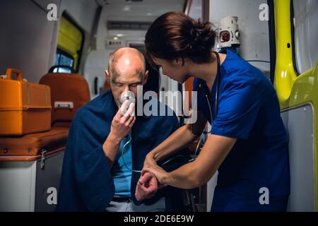 A female paramedic checking her patient's pulse, the patient is having an oxygen mask on. Stock Photo