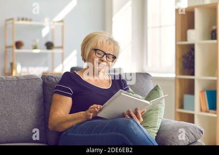 Happy mature woman sitting on couch, enjoying good a book or looking through family photo album Stock Photo