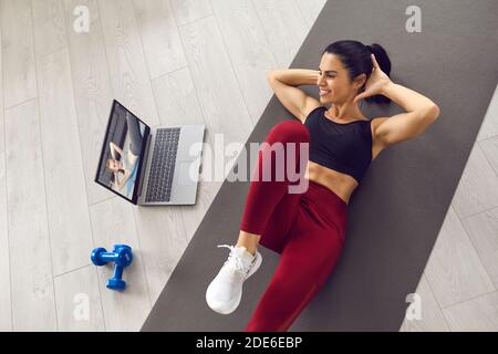 Happy young woman doing crunches at home following instructions from video lesson Stock Photo