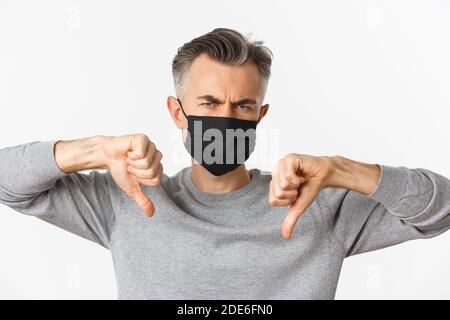 Concept of covid-19, social distancing and quarantine. Close-up of angry and disappointed middle-aged man in black medical mask, frowning upset and Stock Photo