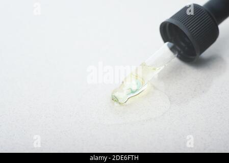 A pipette from cosmetic glass dropper with a little drop of hyaluronic acid, natural serum on its end on the beige background. Stock Photo