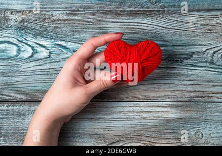A woman holds a heart in one hand over a blue-gray wooden table. Stock Photo