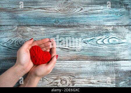 A woman holds a red heart on a blue-gray wooden background. Stock Photo