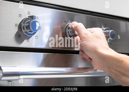 a man's hand turns the toggle switch on the stove. Stock Photo