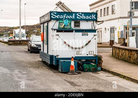 A mobile food trailer marked "Seafood Shack" stands at the pier in Killybegs, County Donegal, Ireland. Green fishing net gear and a shell garland hang on its outer wall. Stock Photo