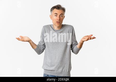 Image of confused middle-aged man shrugging shoulders, looking clueless at camera, standing over white background Stock Photo