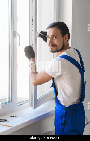 Male repairer in overalls installs a window and poses at the camera Stock Photo
