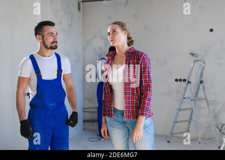 The woman talks to the workman in overalls about the renovation of her apartment. She shows where to make repairs Stock Photo