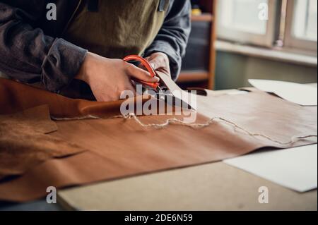 At the masterclass for the production of shoes, an experienced shoemaker cuts out leather with scissors. Stock Photo