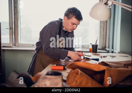 A young old-school shoemaker fulfills an order to make an exclusive leather product. Portrait in the studio. Stock Photo