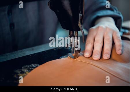 The process of stitching two pieces of genuine leather by a shoemaker on a special old-school sewing machine. Stitches of thread and the hand of the master. Stock Photo