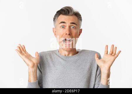 Close-up of scared middle-aged man, looking startled, jumping and screaming frightened, standing ambushed over white background Stock Photo