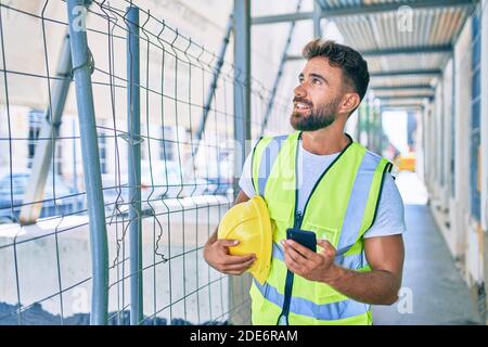 Young hispanic architect man holding blueprint using smartphone at street of city Stock Photo