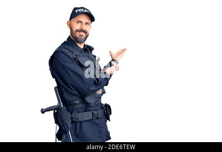 Young handsome man wearing police uniform inviting to enter smiling natural with open hand Stock Photo
