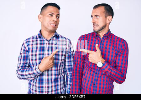 Young gay couple of two men wearing casual clothes pointing aside worried and nervous with forefinger, concerned and surprised expression Stock Photo