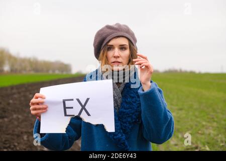 Beautiful sad girl holding half burned white paper with printed text Ex about broken up, divorce with boyfriend, husband Stock Photo