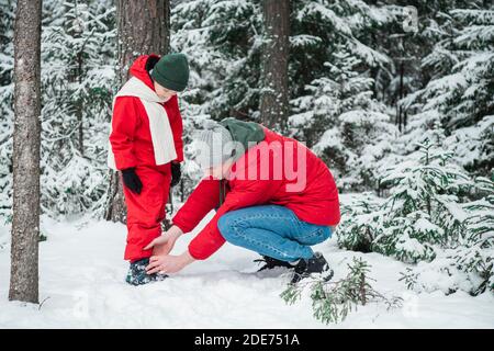 The boy's shoes are unbuttoned, the man from zips up in the winter forest during a walk. Stock Photo