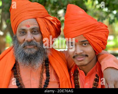 Two Indian Hindu holy men (Shaivite sadhus, monks, devotees), old and young, wear orange outfits and pose together during Maha Shivaratri. Stock Photo