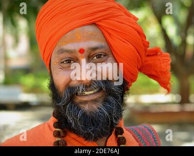 Positive optimistic happy young Indian holy man (sadhu, baba, monk) with orange turban and rudraksha beads around his neck smiles for the camera. Stock Photo