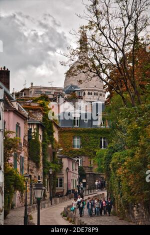 Paris, France - September 17, 2019: People walking along a beautiful street in the Montmartre district, with the Basilica of the Sacred Heart in the b Stock Photo