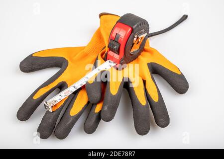 Metal measuring tape with protective gloves. Accessories for carpenters to measure. Light background. Stock Photo
