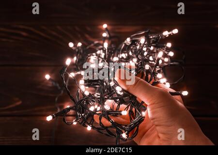 Woman hand holds shining christmas lights garland in a darkness. Glowing LED lightning in a palm. Winter season holidays Christmas and New Year. Stock Photo