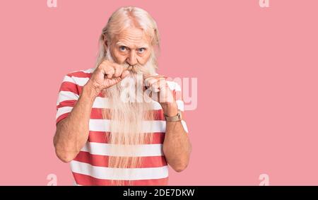 Old senior man with grey hair and long beard wearing striped tshirt ready to fight with fist defense gesture, angry and upset face, afraid of problem Stock Photo